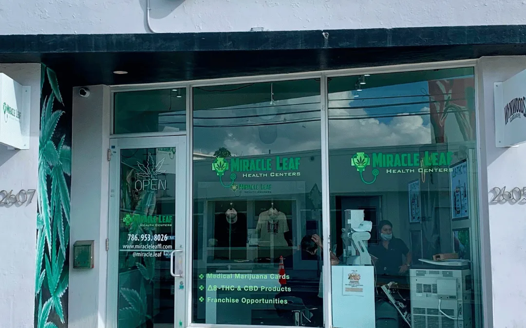 The Miracle Leaf® Health Centers clinic at 2607 N Miami Avenue, Wynwood: a white single-storey unit with a full-height glass frontage, the leaf logo across the window, and a painted green mural running down the left of the entrance.