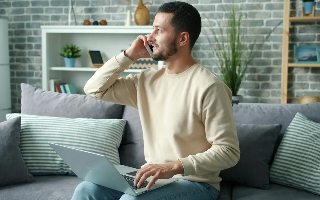 A man on a sofa with a laptop open, talking on the phone.