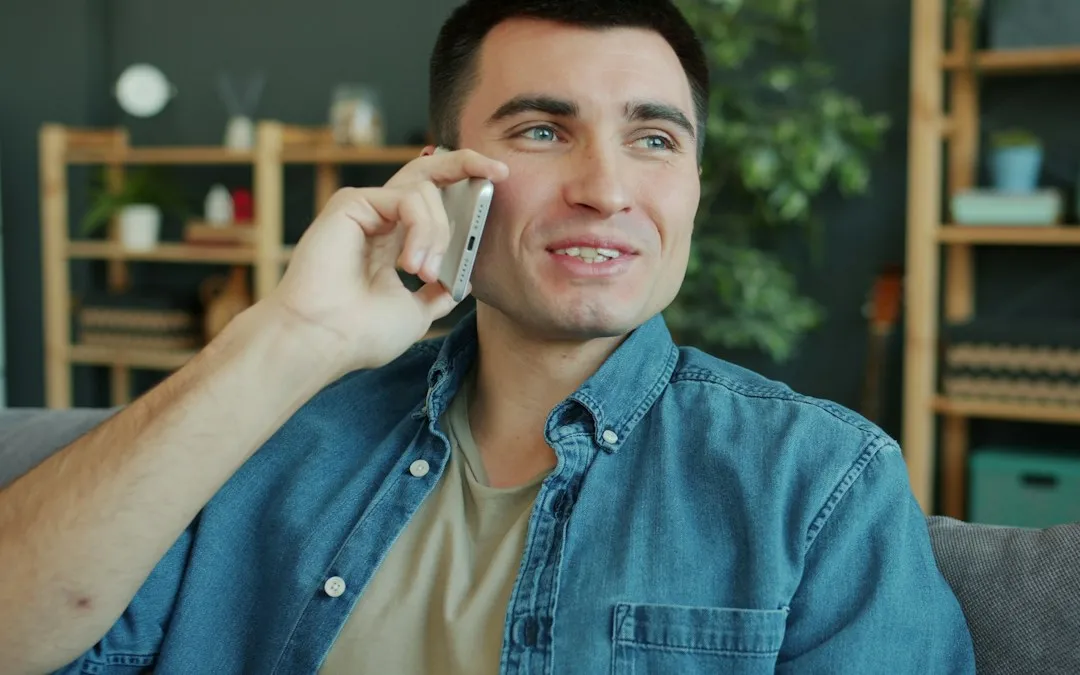 A man at home in a denim shirt, on a phone call.