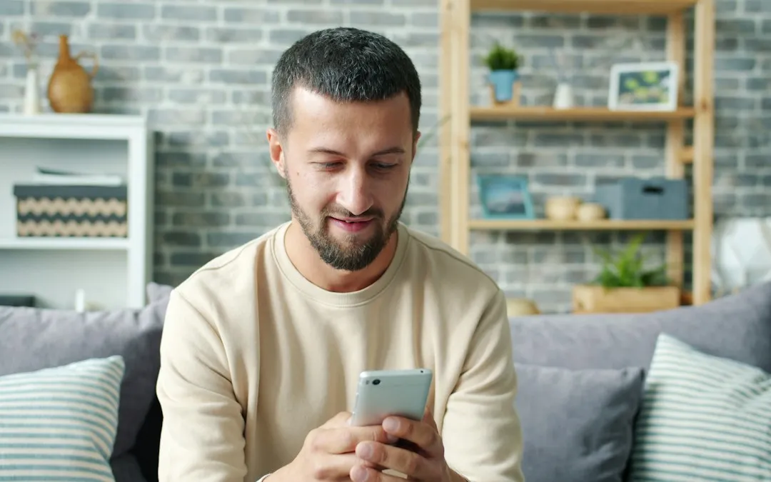 A man on a sofa at home, reading something on his phone.